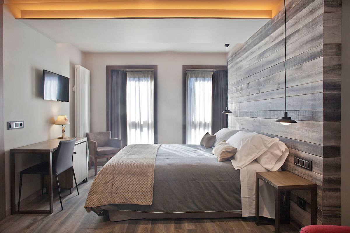 Un dormitorio moderno con una cama grande, un escritorio con lámpara y un televisor en la pared.