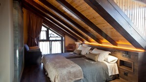 Une chambre avec un plafond en pente, des poutres apparentes, un grand lit, une table de chevet et une fenêtre avec des rideaux.