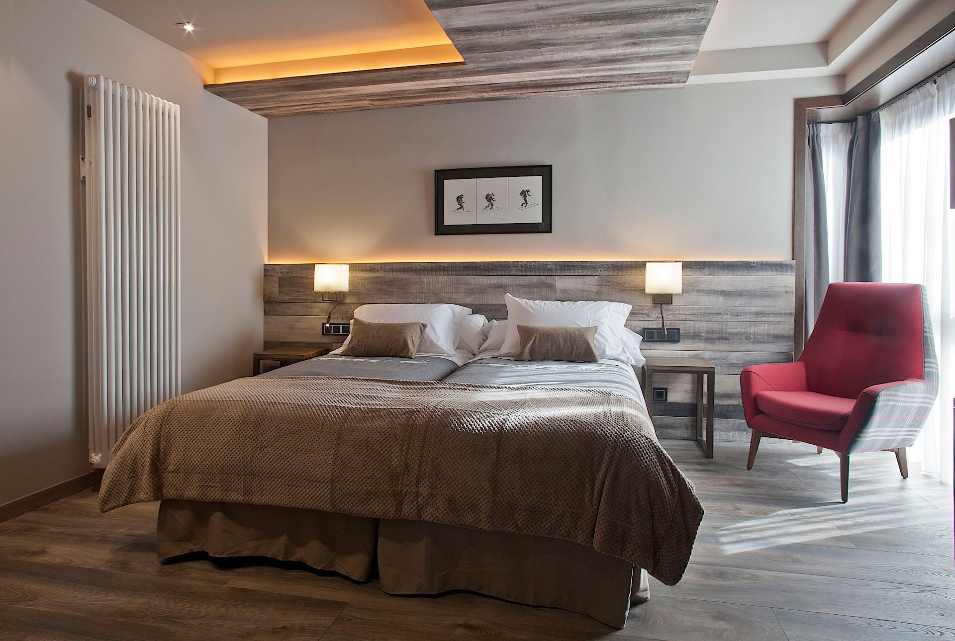 A modern hotel room with a large bed, two bedside tables, a red armchair, and a wooden headboard.