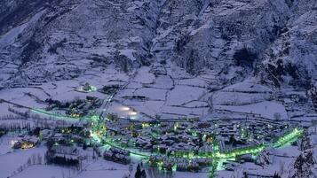 A snow-covered village with buildings and roads illuminated by green lights, surrounded by mountains.