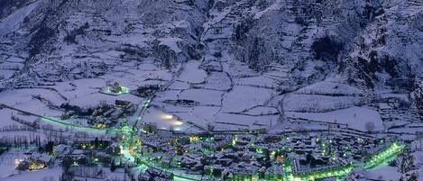 A snow-covered village with buildings and roads illuminated by green lights, surrounded by mountains.