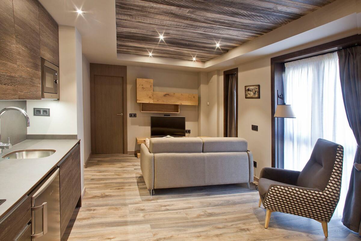 Una sala de estar moderna con un sofá, un sillón estampado, un televisor de pantalla plana y techo de madera.