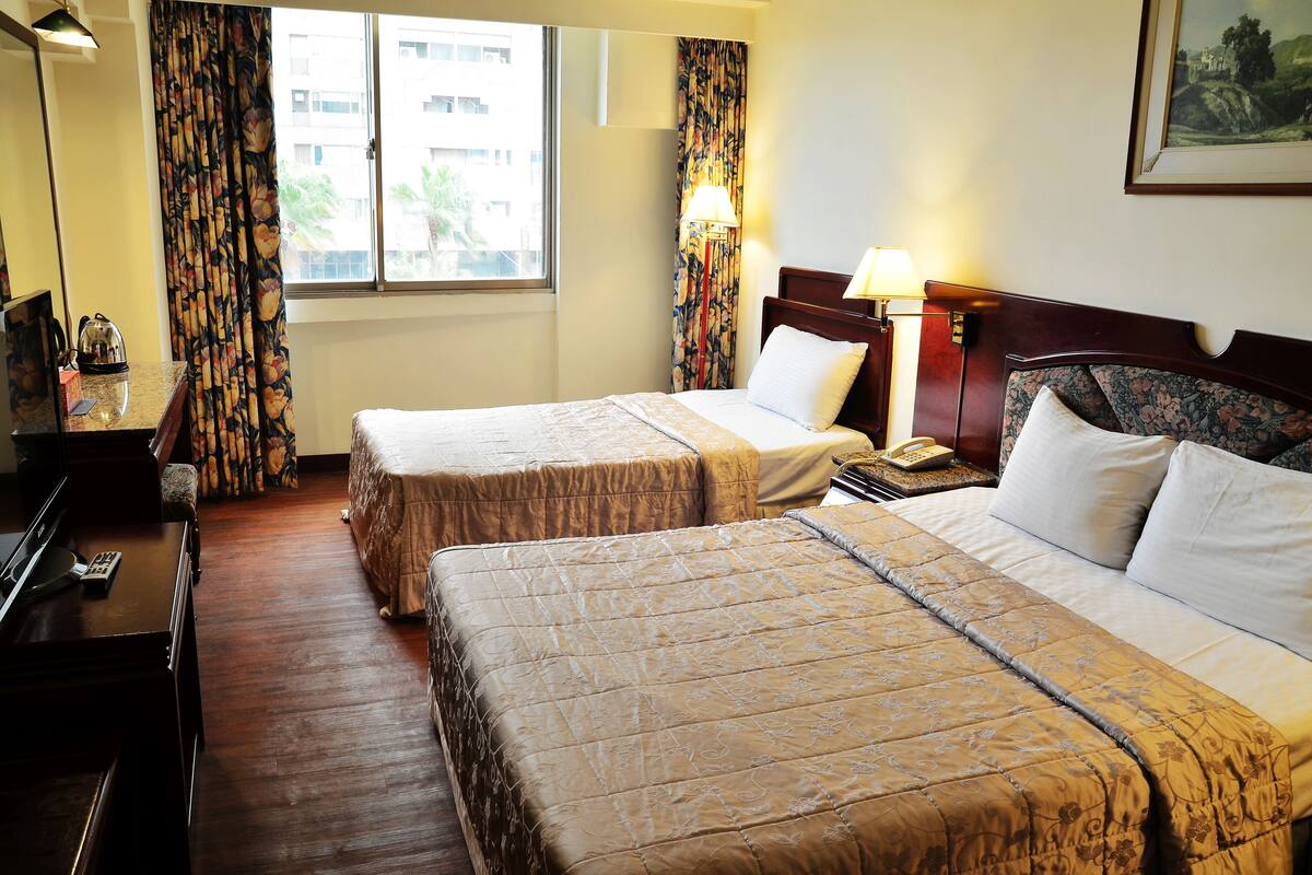 A hotel room with two beds, a desk, a lamp, and a painting on the wall.