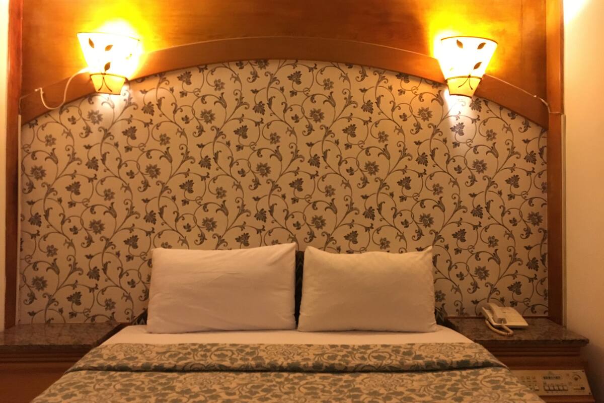 A hotel room with a floral wallpaper, two bedside lamps, a bed with white linens, and a nightstand with a phone.