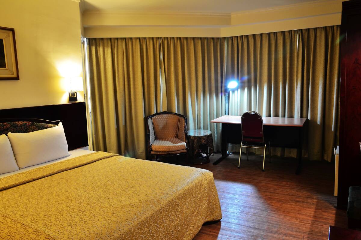 A hotel room with a large bed, a desk, and a chair.
