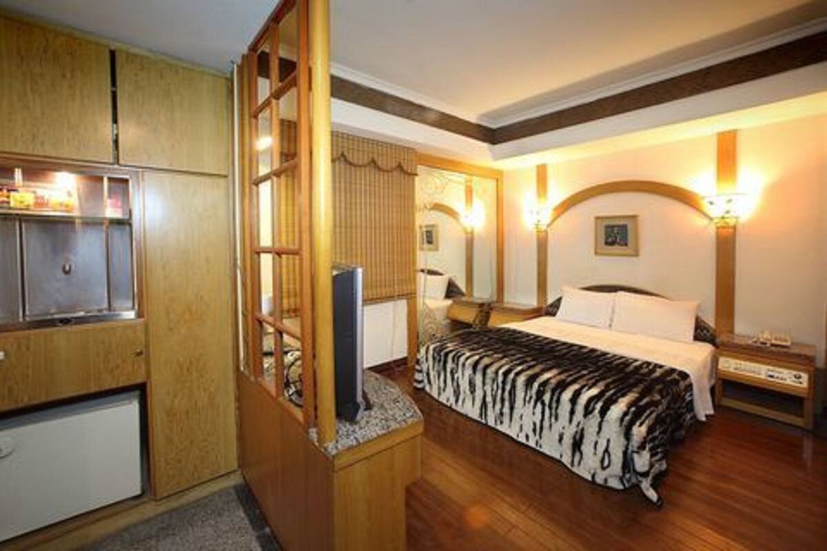 A bedroom with a bed, wooden wardrobe, and a small refrigerator.