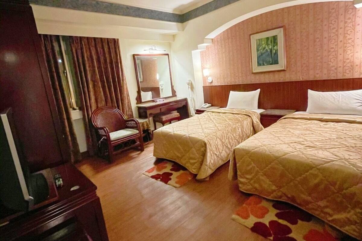 A hotel room with two beds, a desk, a chair, a mirror, and a television.