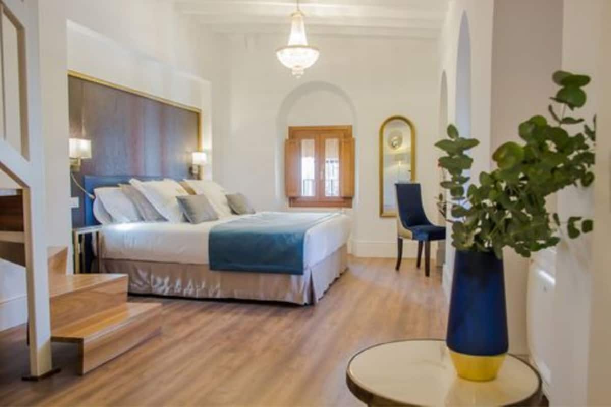 A bedroom with a bed, bedside tables, a chair, a plant, and a staircase.