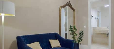 A room with a blue sofa, a round coffee table, a large mirror, and a potted plant.