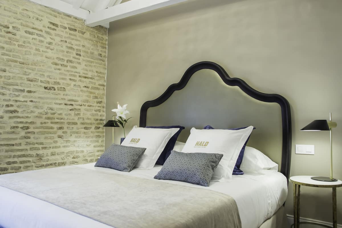 A neatly made bed with white and patterned pillows, a modern headboard, and a small bedside table with a lamp.