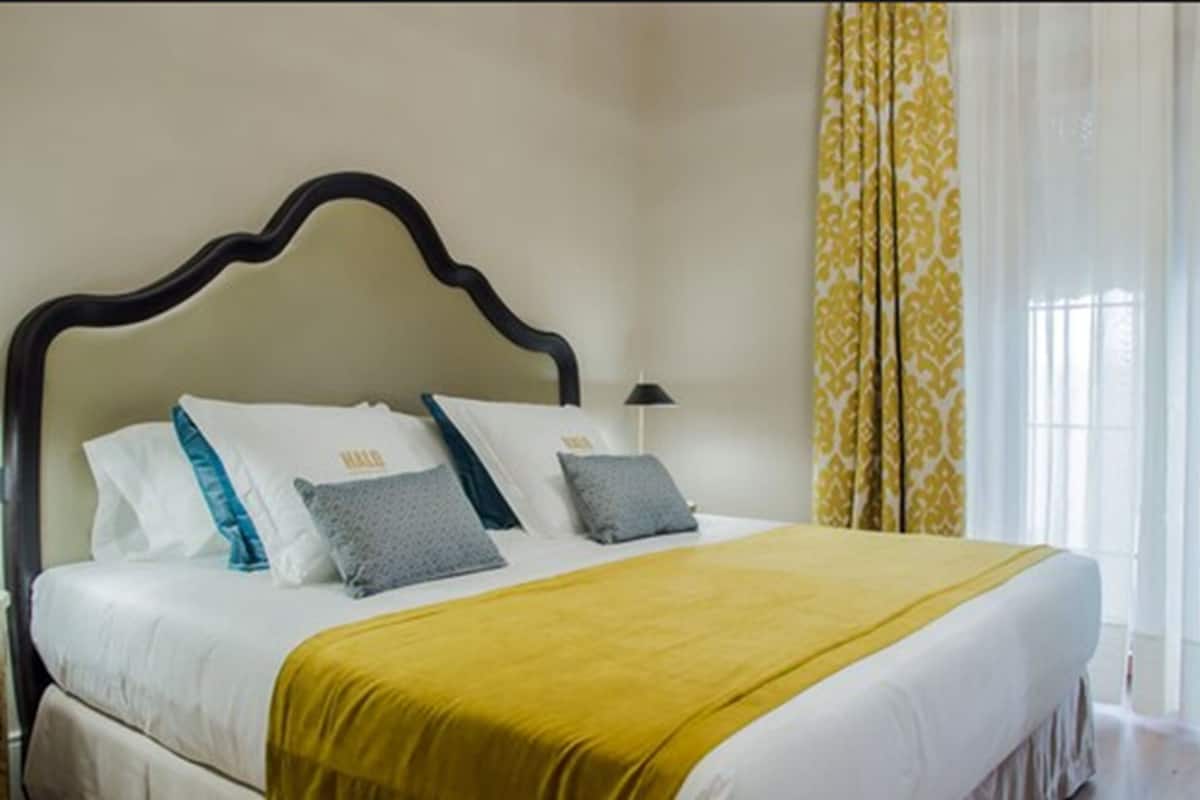 A neatly made bed with a yellow blanket, white bedding, and a dark wooden headboard.
