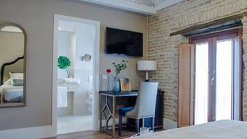 A bedroom with a bed, a desk with a chair, a TV mounted on the wall, and a bathroom visible through an open door.