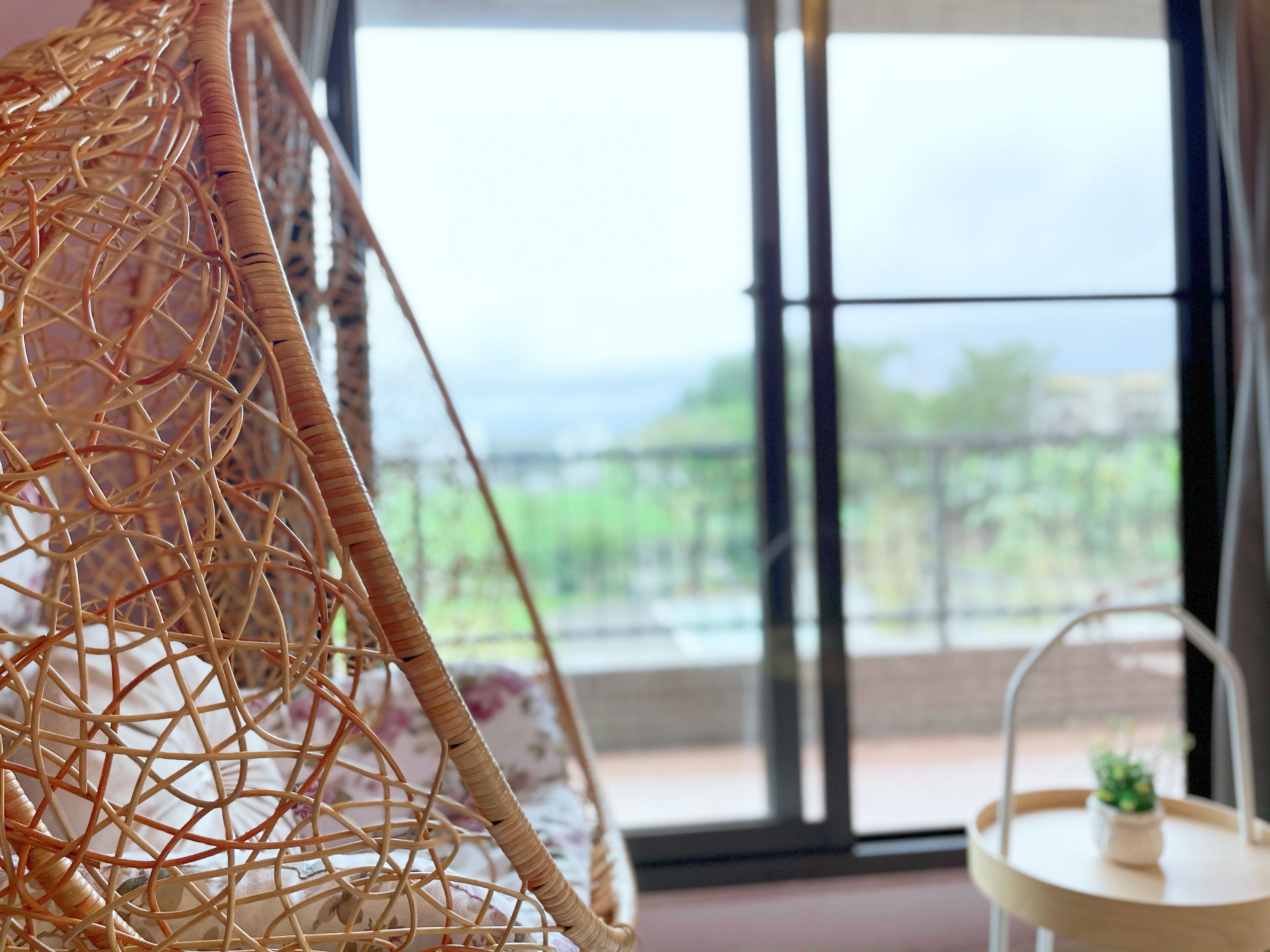 A wicker chair with a view of a balcony and a small table with a plant.