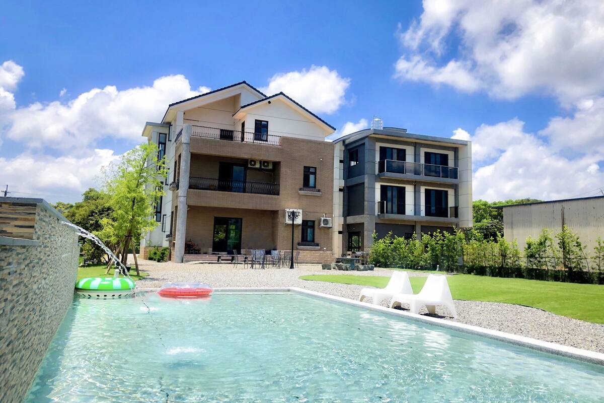 A modern building with a swimming pool, outdoor seating, and a clear sky.