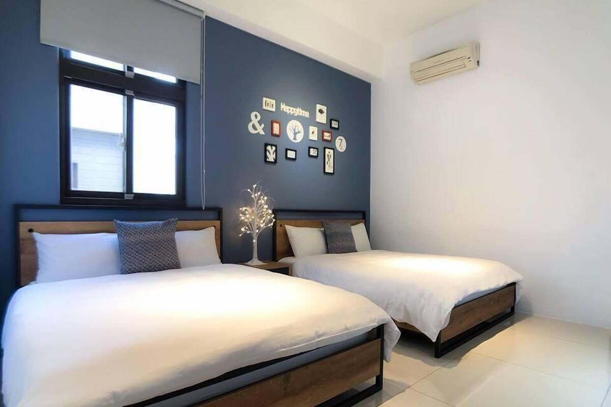 A bedroom with two beds, a wall with framed pictures, and a window.