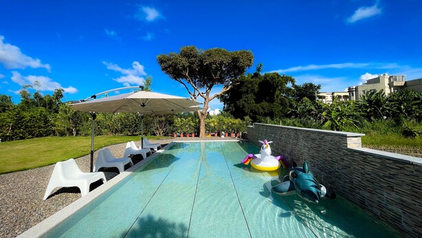 Una piscina con pared de piedra, un árbol y una sombrilla blanca.