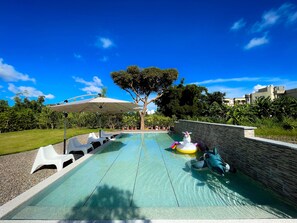 Una piscina con pared de piedra, un árbol y una sombrilla blanca.