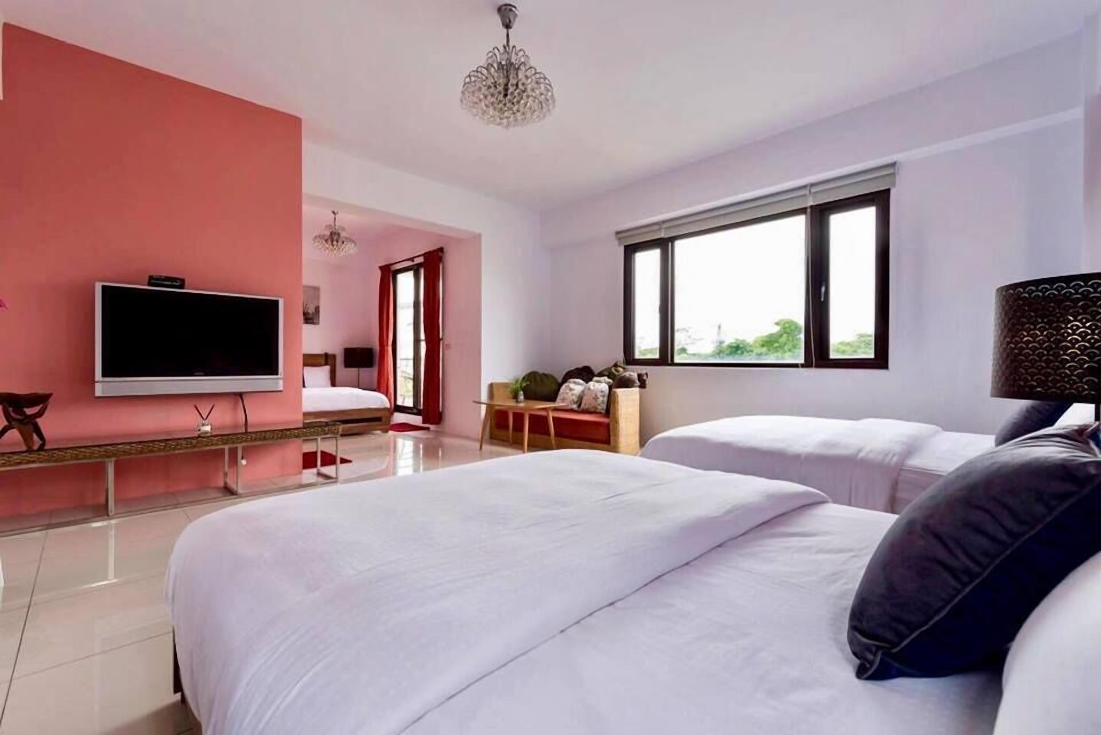 A hotel room with two beds, a TV, a chandelier, and a window with a view.