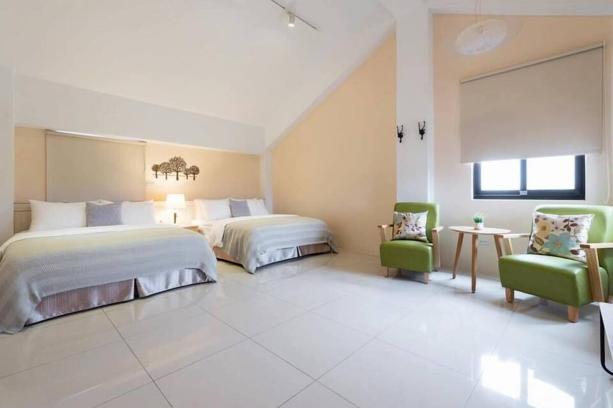 A modern hotel room with a large bed, two chairs, a small table, and a window with a view.