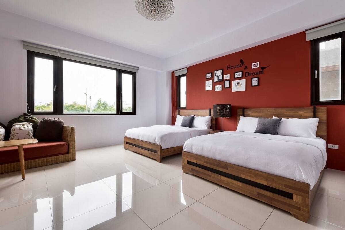 A modern bedroom with two beds, a sofa, and a large window.