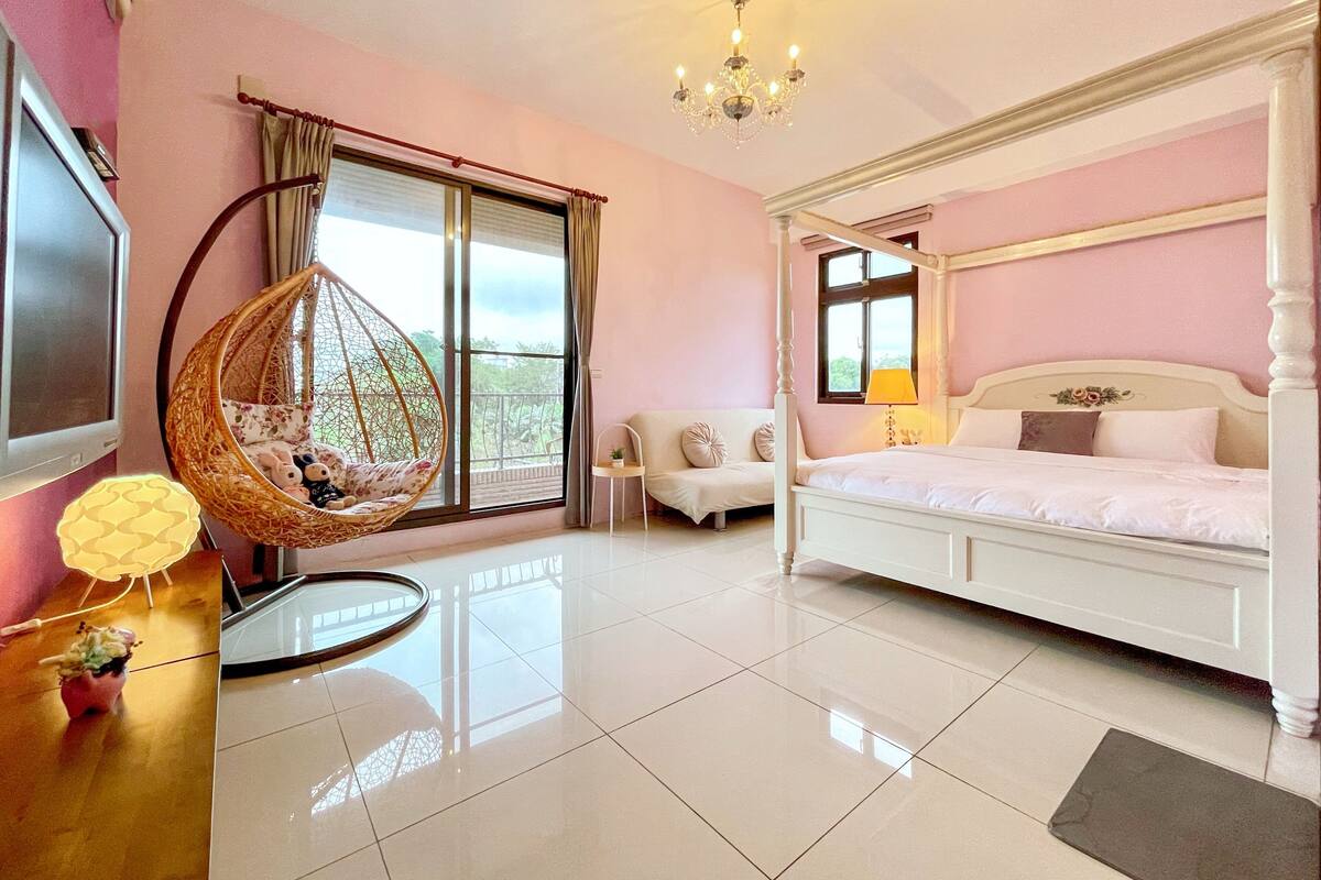 A bedroom with a four-poster bed, a hanging chair, a sofa, and a TV.