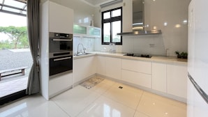 Una cocina moderna con armarios blancos, una campana extractora de acero inoxidable y un ventanal con vistas a árboles.