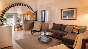 A cozy living room with a sofa, armchair, and coffee table. There is a fireplace, a dining area, and a large window. - Casa da Montanha (Lagos)