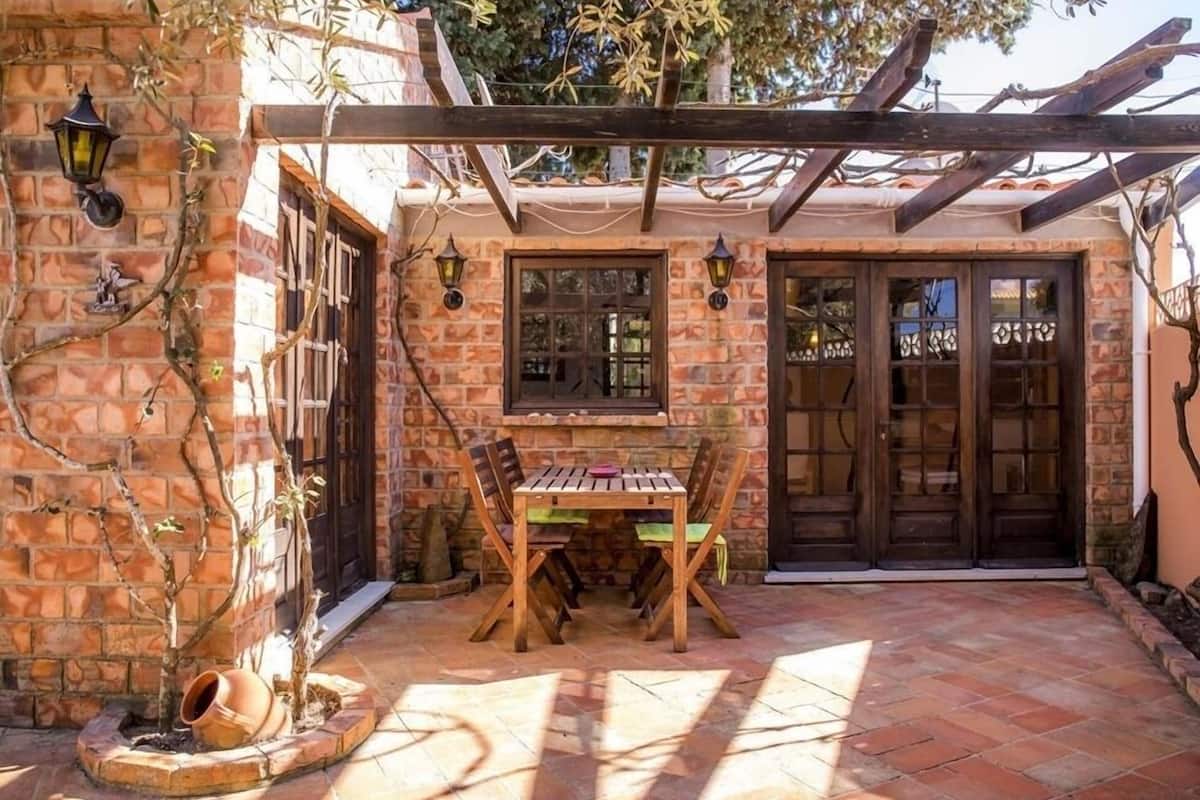 A patio with a wooden table and chairs, surrounded by stone walls and a pergola.