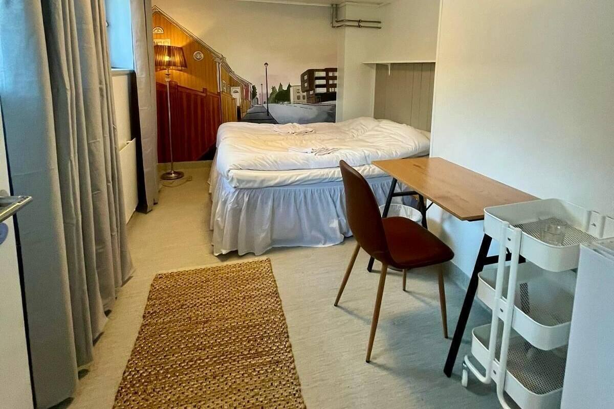 Una habitación de hotel compacta con cama, escritorio, silla, una mesita y espacio para guardar objetos.