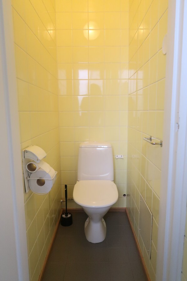 A small, narrow bathroom with yellow tiled walls, a white toilet, and a toilet paper holder.