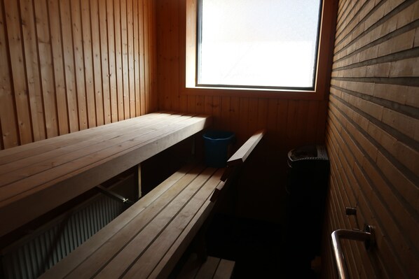 Un cuarto de sauna con bancos de madera, un bote de basura azul y una ventana.
