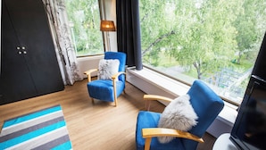 A modern room with a large window, two blue armchairs, a wooden floor, and a striped rug. - Hostel Villa Kemi (Kemi)