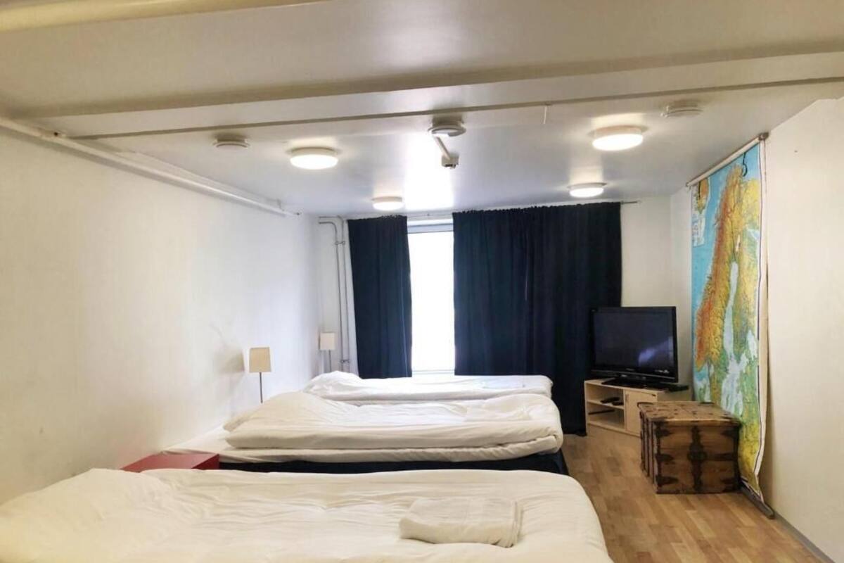 Una habitación de hotel con dos camas, un televisor, un mapa en la pared y un cofre de madera.