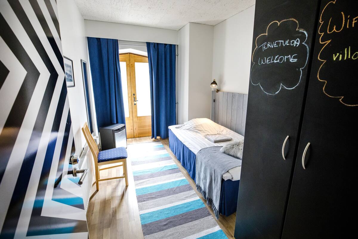 Una habitación de hotel moderna con cama, escritorio y armario. Hay una pizarra con la palabra “Welcome” escrita.