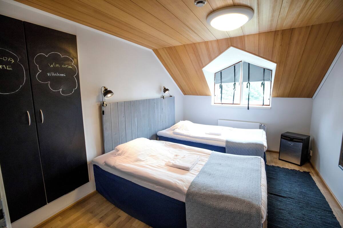 Un dormitorio con dos camas, un armario, un escritorio, una lámpara y una ventana con vistas.