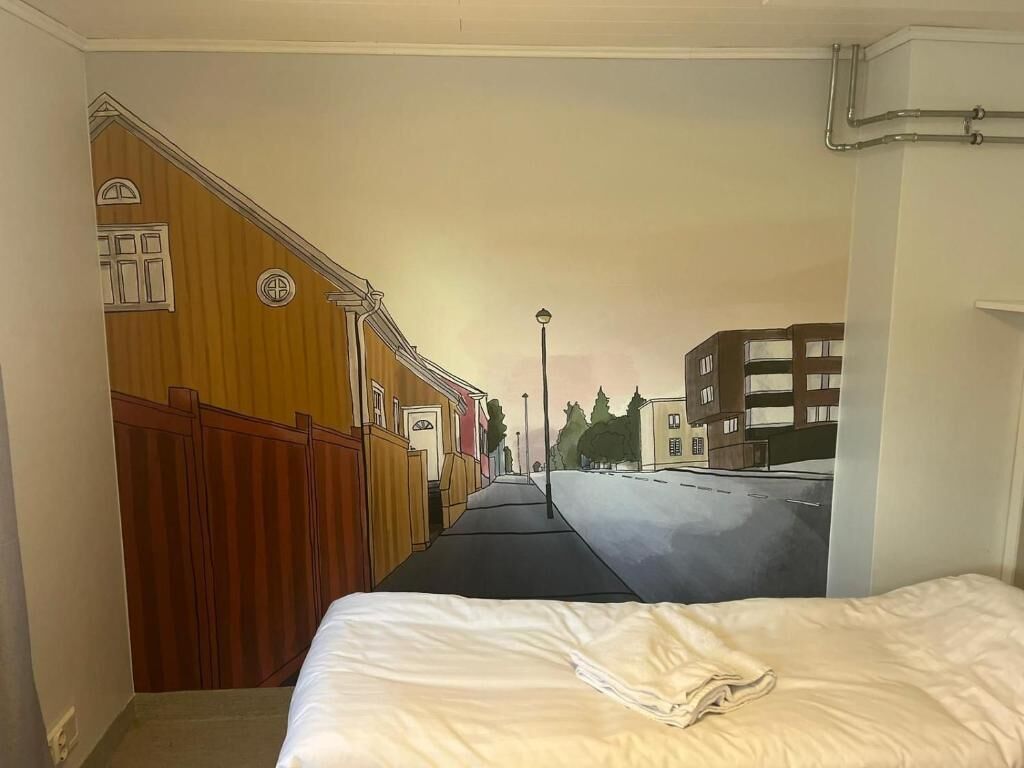 Un dormitorio con una cama, un mural en la pared que muestra una escena callejera y una ventana con persianas.