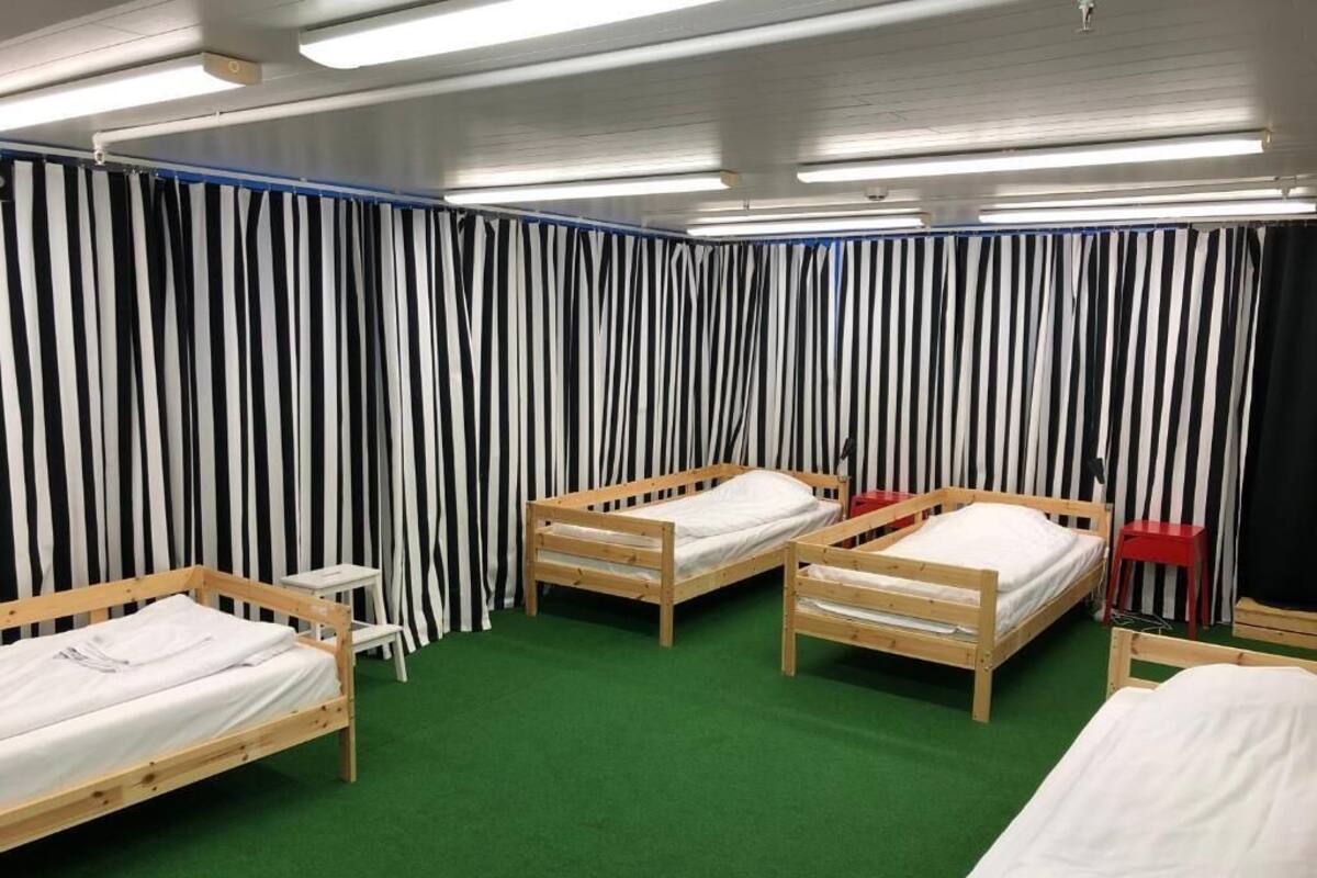 Una habitación con cuatro camas de madera, alfombra verde y cortinas a rayas.