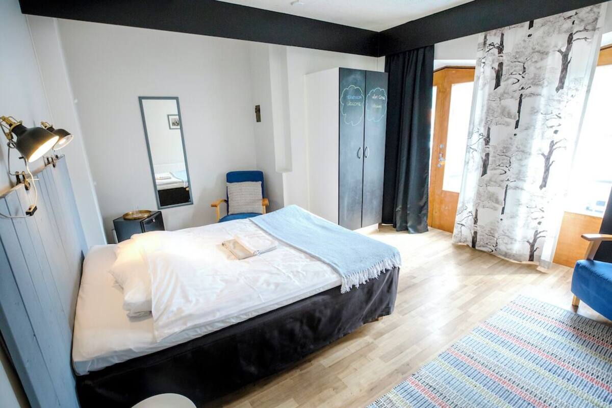 Un dormitorio con cama, una silla, armario, espejo y ventana con cortinas.