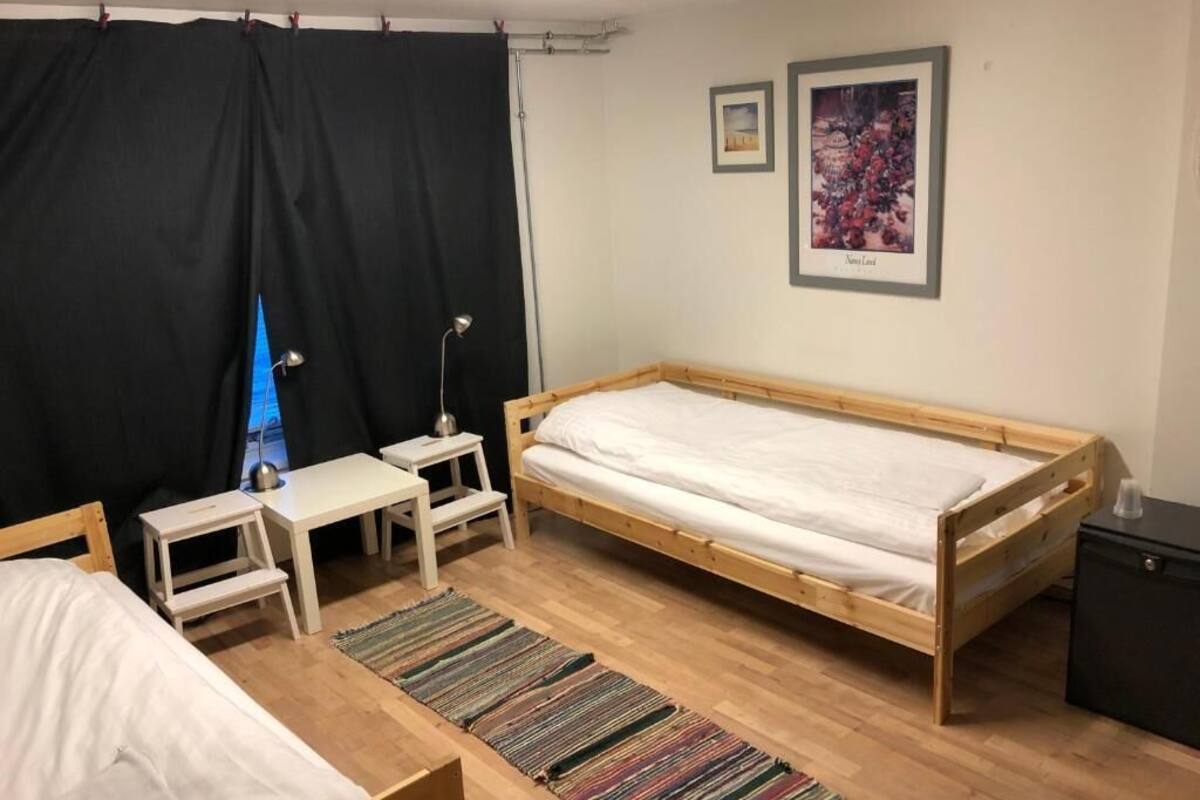 Una habitación con una cama de madera, un escritorio pequeño, una silla, una mesita de noche, una cortina negra y un cuadro enmarcado en la pared.