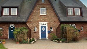A two-story brick house with a steeply pitched roof, a central entrance with a blue door, and two side entrances with blue doors. - Ferienhaus Weetstich (Sylt)