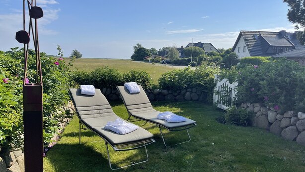 Two lounge chairs with towels, a stone wall, and a white picket fence in a garden setting. - Ferienhaus Weetstich (Sylt)