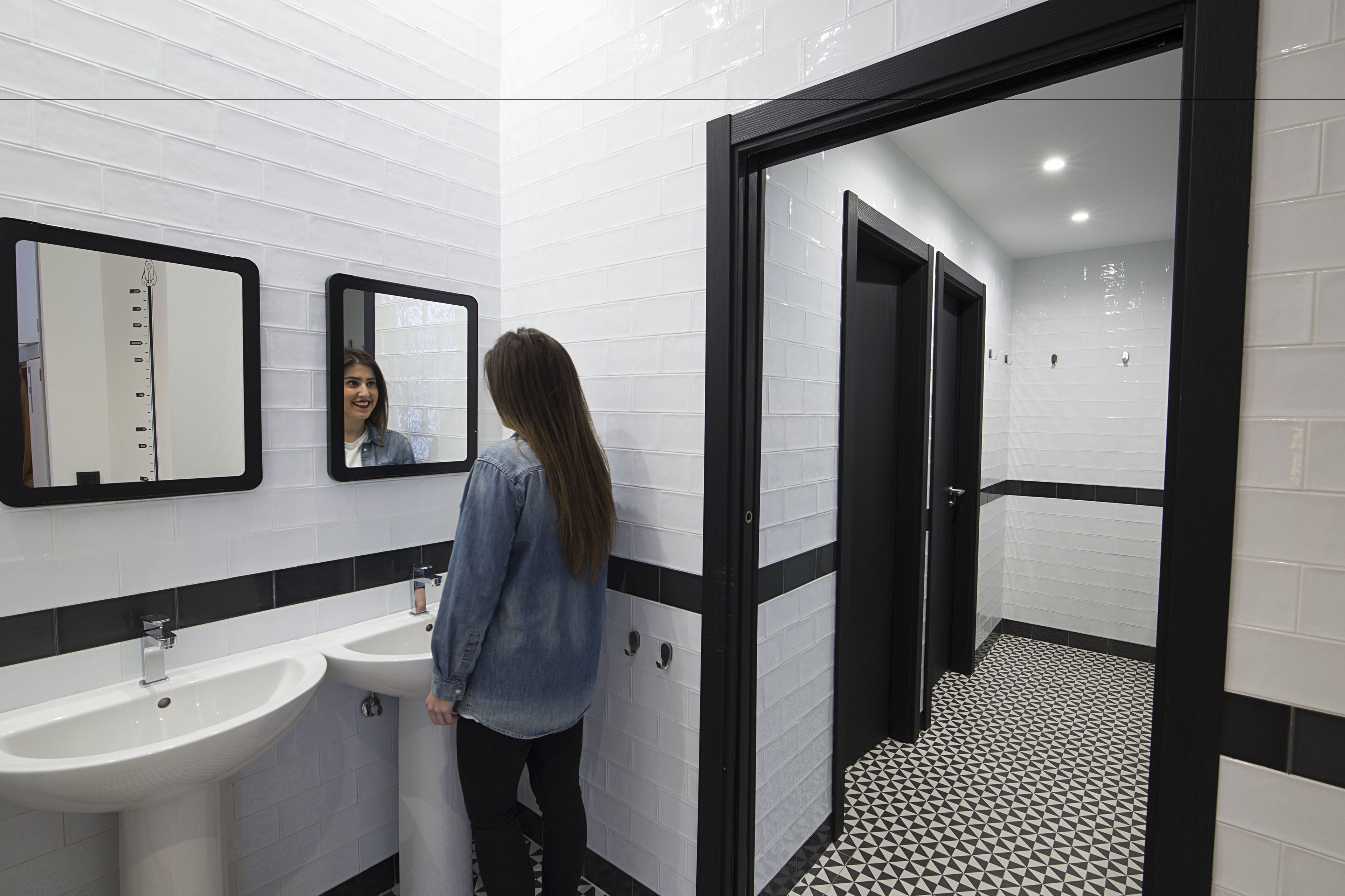Une salle de bain avec deux lavabos, un miroir et une porte à cadre noir donnant sur une autre pièce.