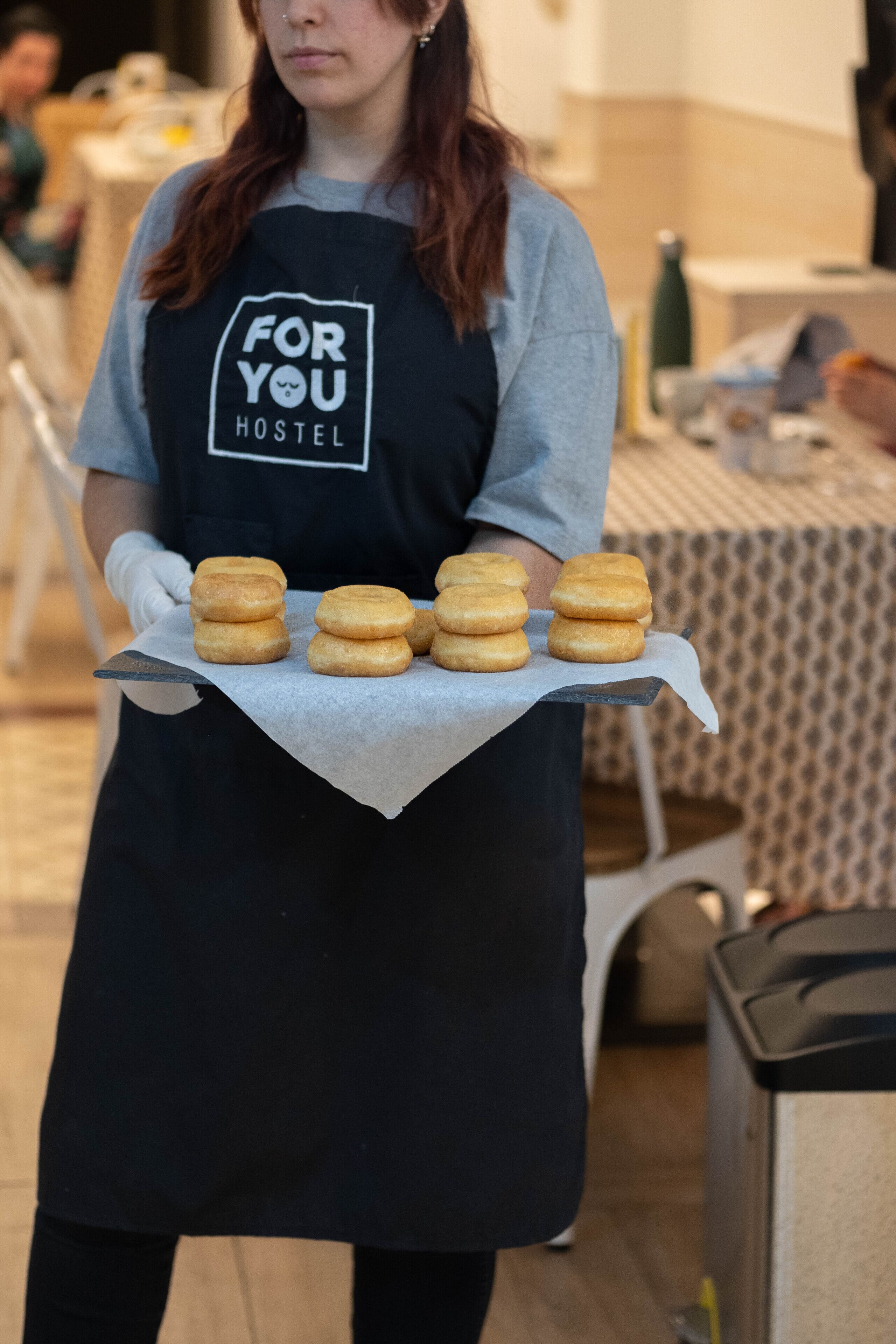 Een persoon in een zwarte schort met een logo, die een dienblad met verschillende ronde gebakjes vasthoudt.