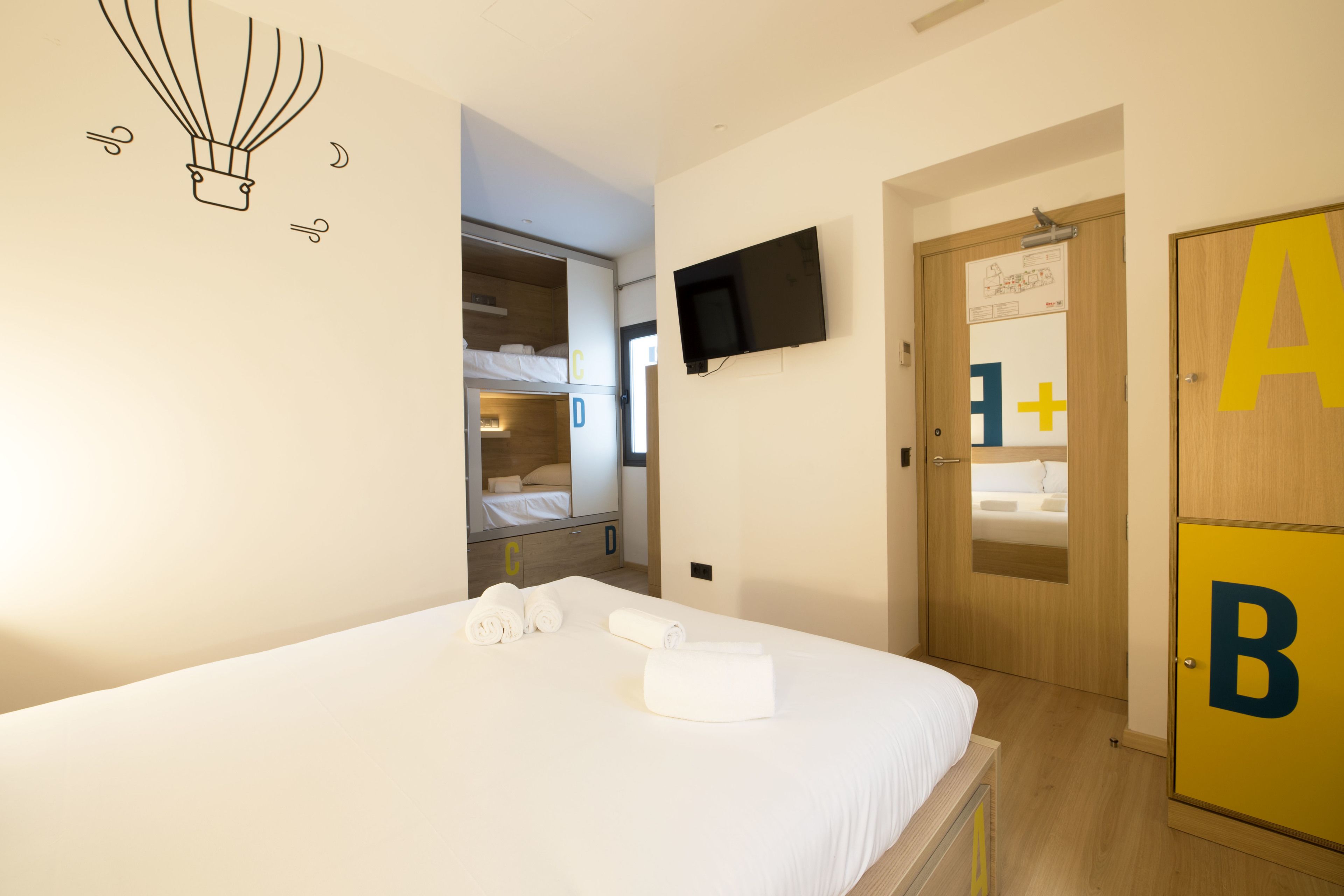 Ein Hotelzimmer mit einem Bett, einem an der Wand montierten Fernseher und einem Schrank mit großen Lettern.