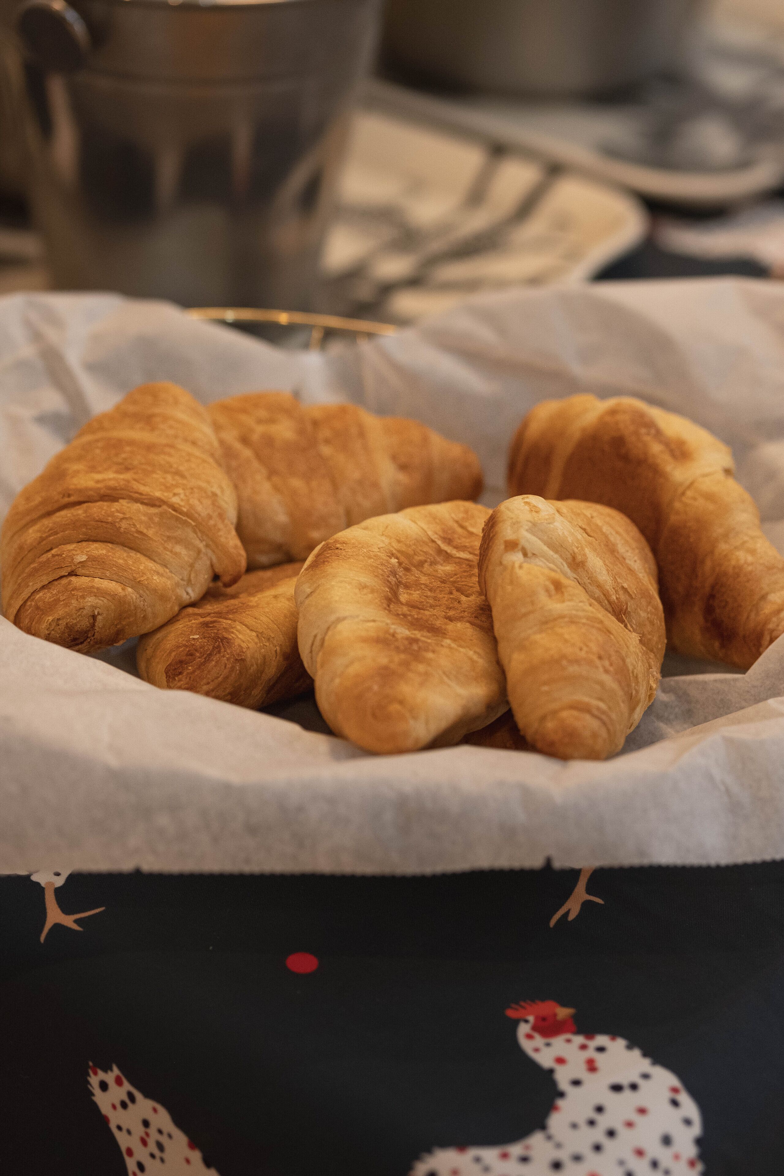 Un cistell de croissants damunt un taulell amb drap negre i un disseny de gall.
