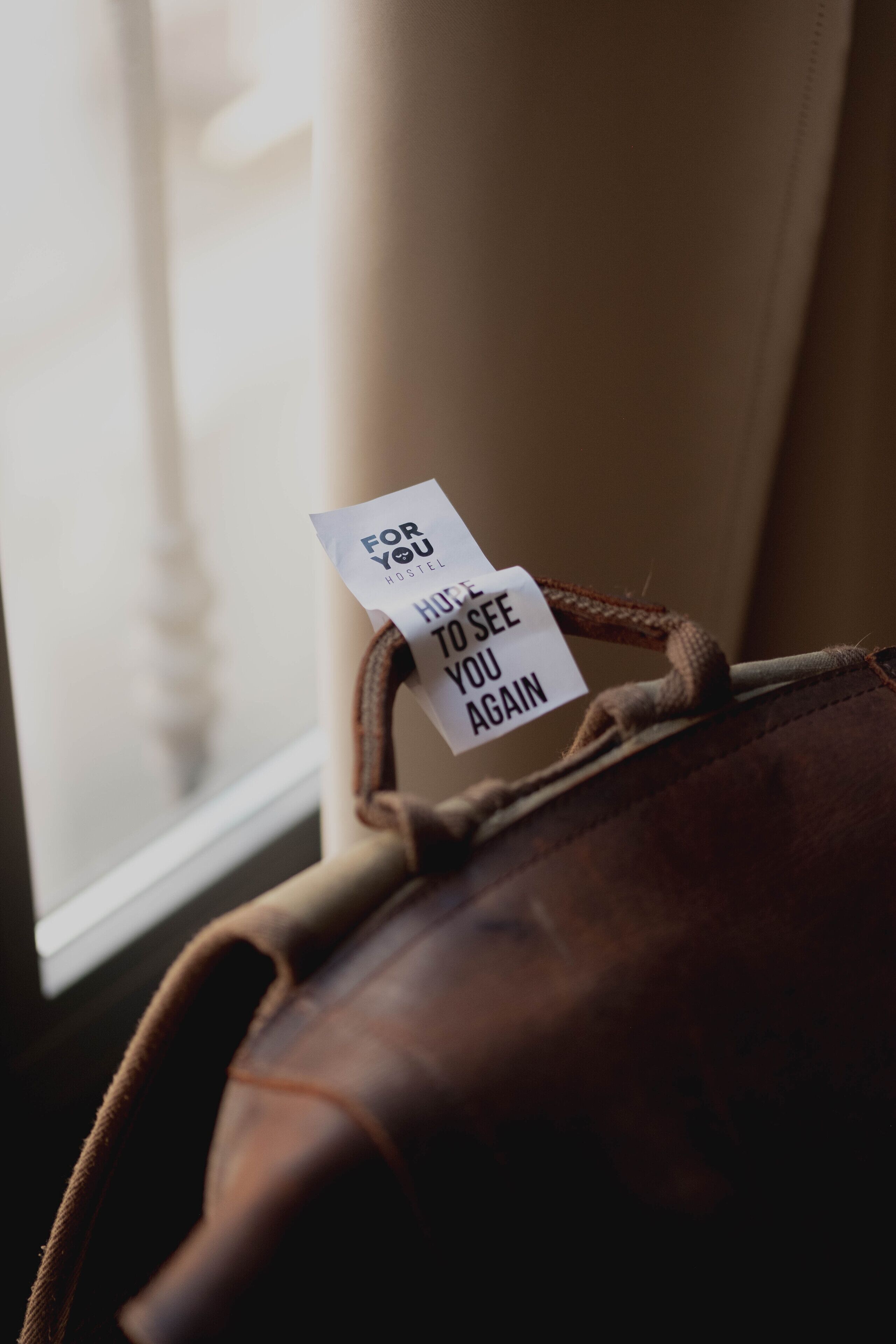 Una bolsa de cuero marrón con una etiqueta que dice 'For You Hostel' y 'Hone To See You Again'.