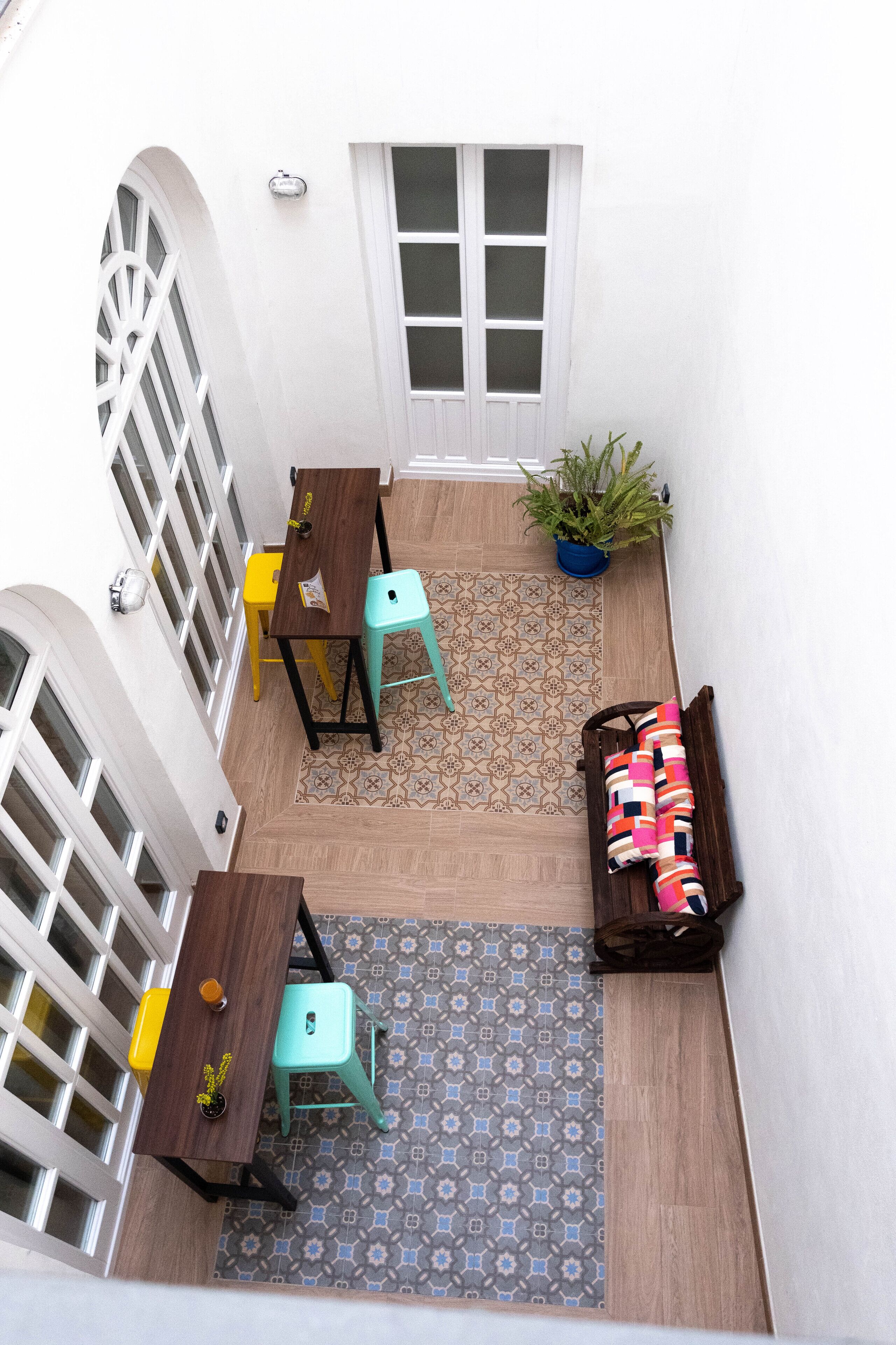 A small patio area with a wooden table, two chairs, a bench, and a potted plant.
