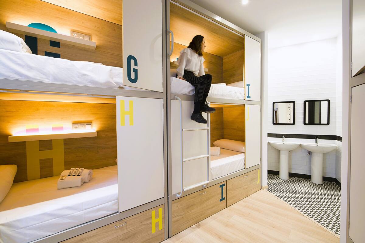 Ein modernes Hotelzimmer mit Stockbetten, einem Badezimmer mit zwei Waschbecken und einem Holzboden.