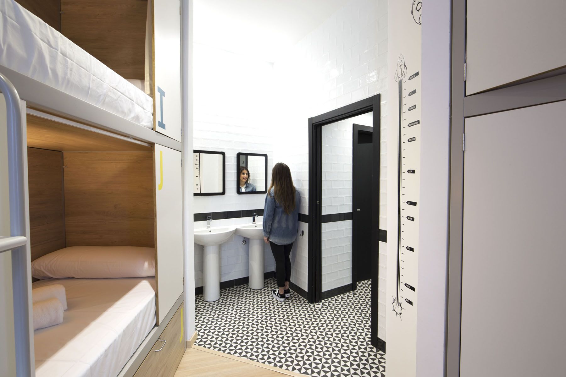 A compact hotel room with a bunk bed, a small sink, and a mirror.