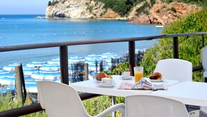 A seaside table with breakfast items, overlooking a coastal view with umbrellas and a castle on a hill.